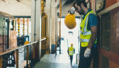 Worker in safety gear holding a hard hat in an industrial facility.