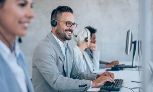 A cheerful man in a call center, equipped with headphones, providing assistance to a client over the phone.