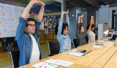 Four people sitting at a conference table in an office, stretching their arms upwards.